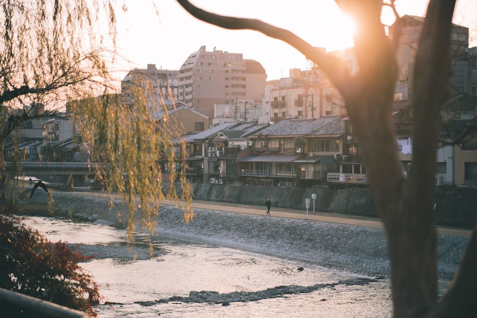 A serene view of a cityscape along a riverbank with warm sunset light and urban architecture.