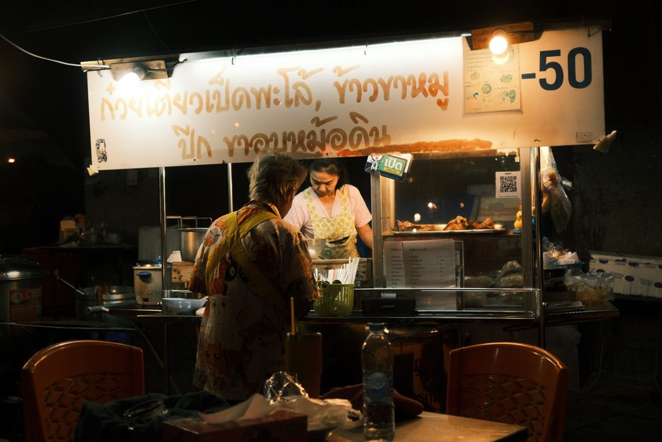 A bustling night scene at an urban food stall with people ordering food.