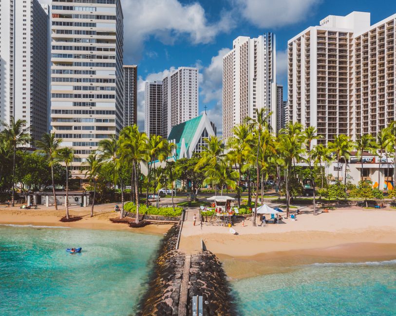 Explore the vibrant Honolulu coastline with skyscrapers, palm trees, and a sandy beach under a sunny sky.