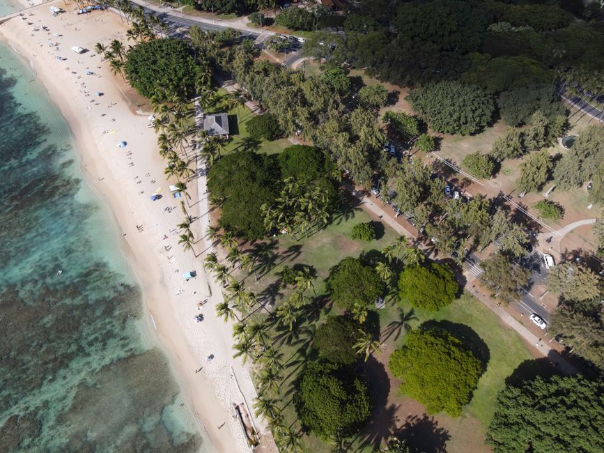 Aerial view of a beautiful tropical beachfront with clear water and lush greenery.
