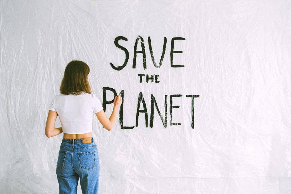 Back view of a woman with brown hair writing 'Save the Planet' on a white background with 