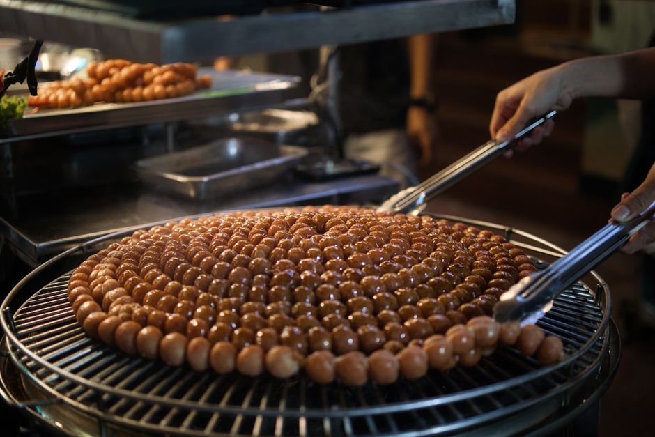 Close-up of sausages being grilled in a spiral pattern at a street food market.
