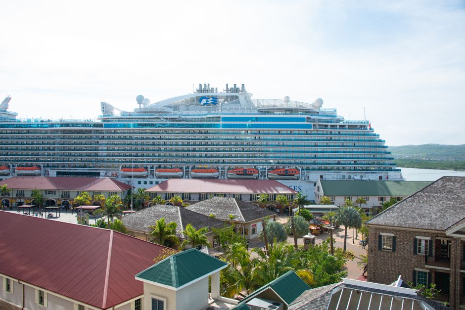 Luxurious cruise ship docked in tropical harbor amidst vibrant buildings.