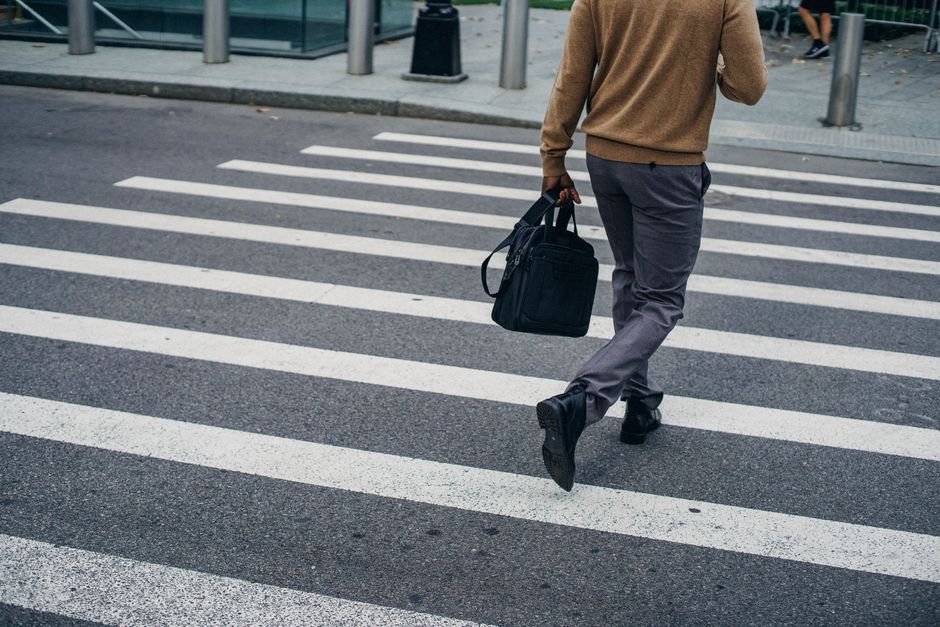 Crop back view of black male pedestrian with bag on crosswalk in city center