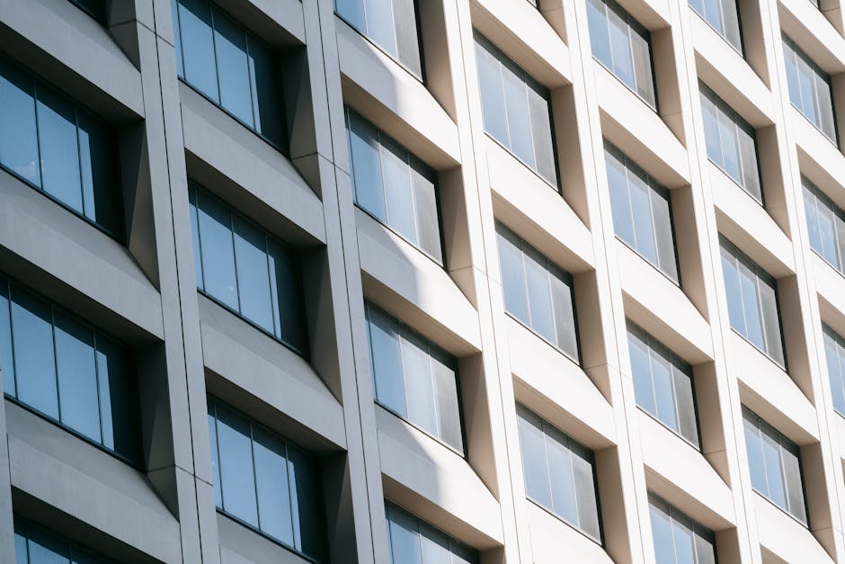Low angle of rows of modern glass windows on facade of contemporary white multistory building reflecting sunlight