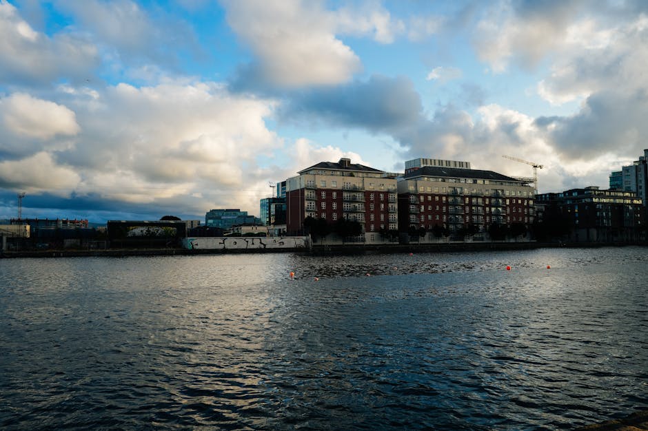 Scenic view of a city waterfront with striking clouds overhead, reflecting in the water.