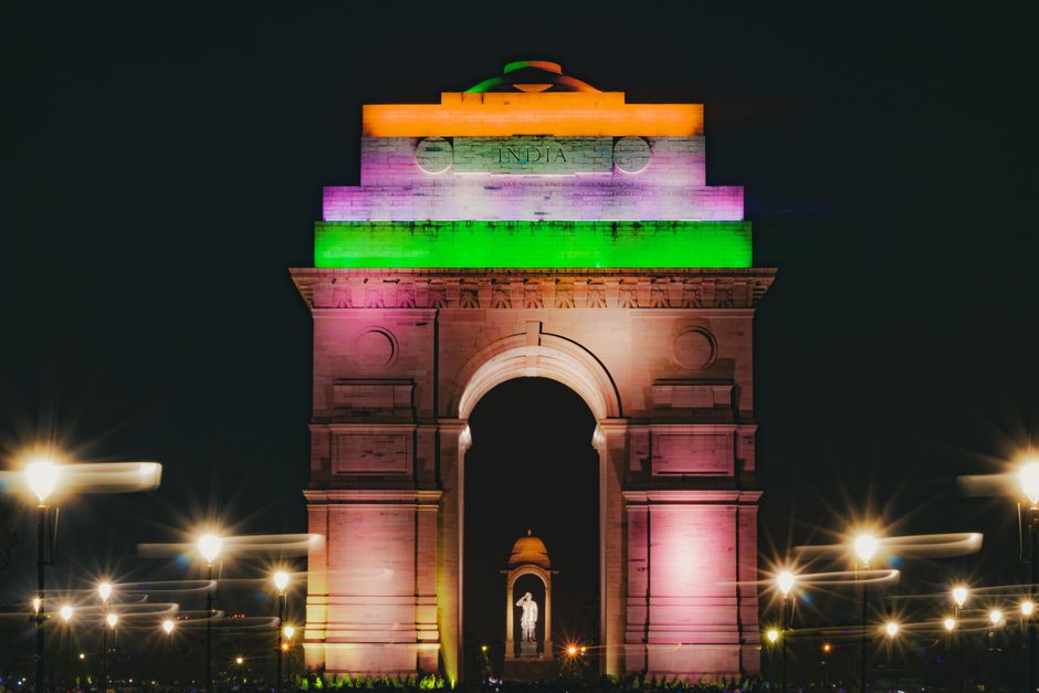 A vibrant night view of the India Gate in Delhi, beautifully lit in the colors of the Indian flag.