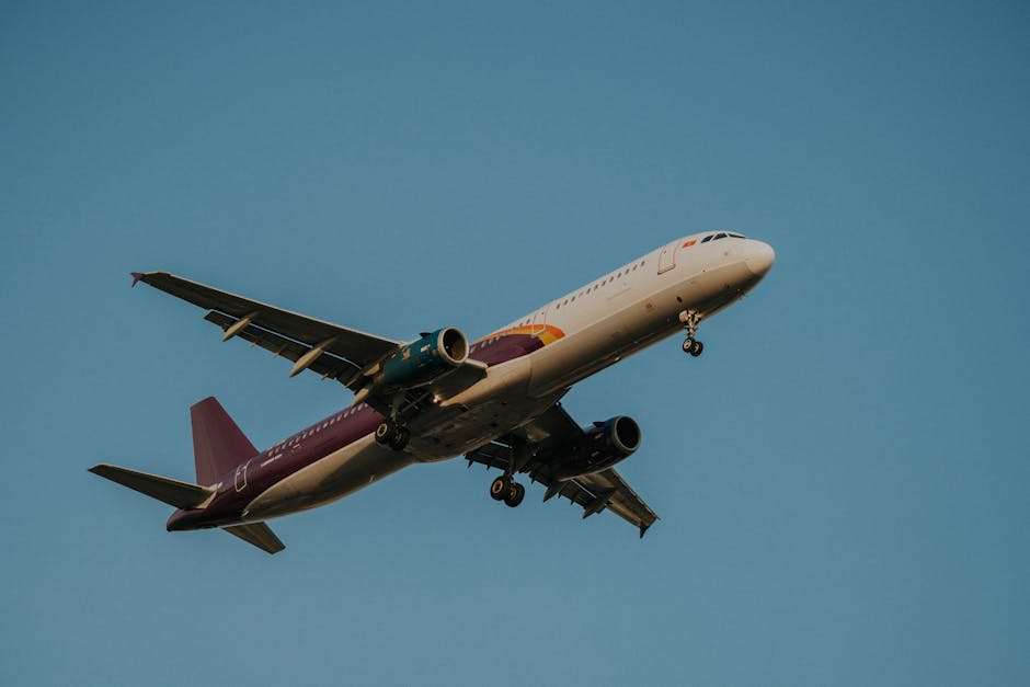 Low-angle view of a commercial airplane flying against a clear blue sky, showcasing its wings and fuselage.