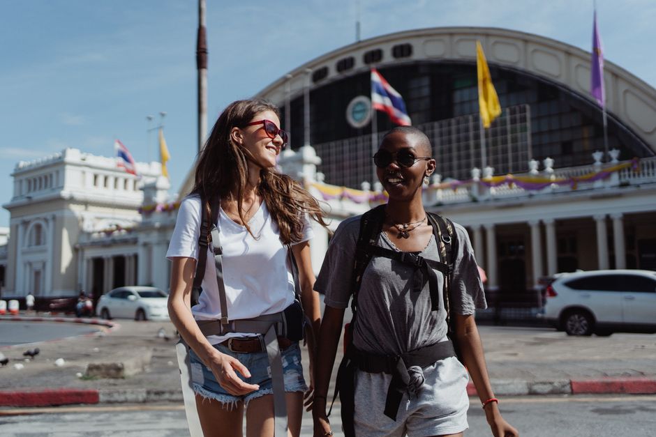 Two women walking joyfully in front of a historic building, enjoying a sunny day in the city.