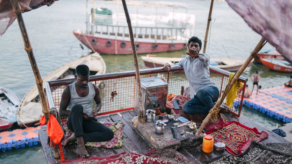 Two men engaged in daily activities on a boat by the Ganges River in Varanasi, India.