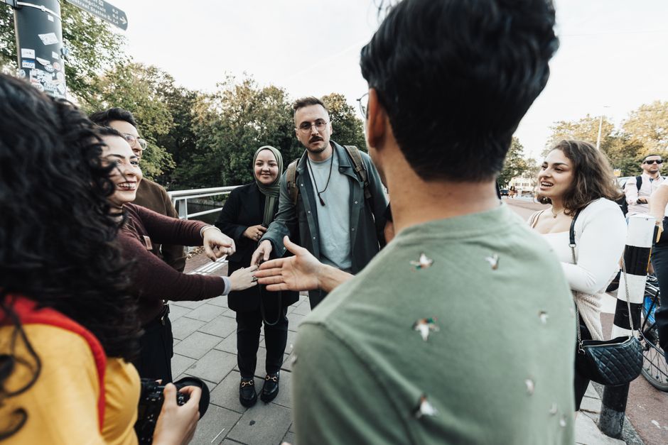 A diverse group of adults engaging in a lively conversation outdoors on a sunny day.