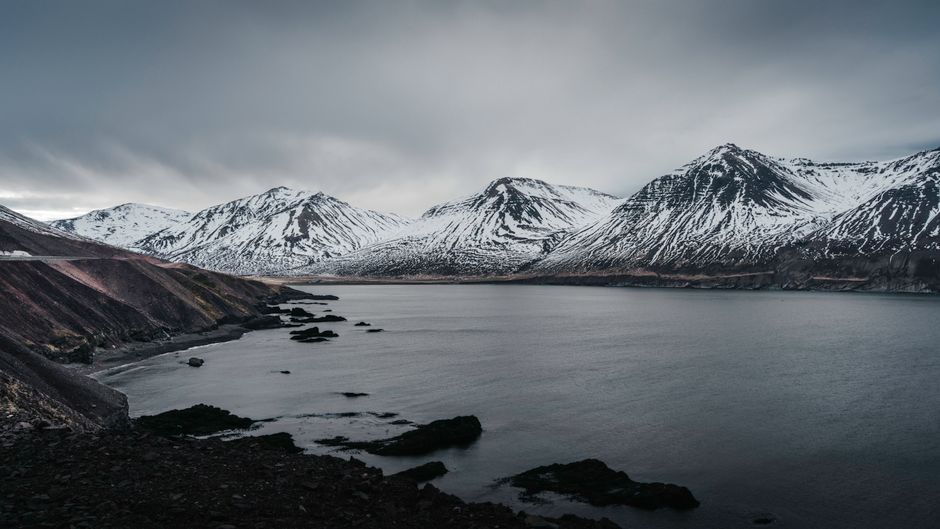 Striking snow-covered mountains by the Icelandic coast under a cloudy sky, showcasing natural beauty.