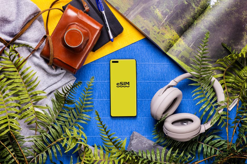 Flat lay of technology and travel essentials with a smartphone featuring eSIM on a colorful background.