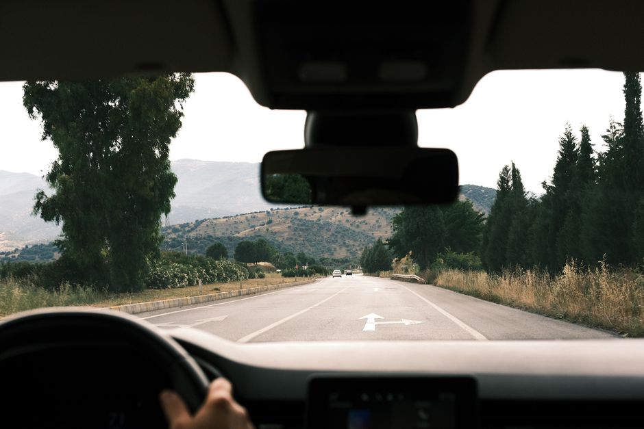 View from inside a car driving on a scenic, mountainous road during daytime.
