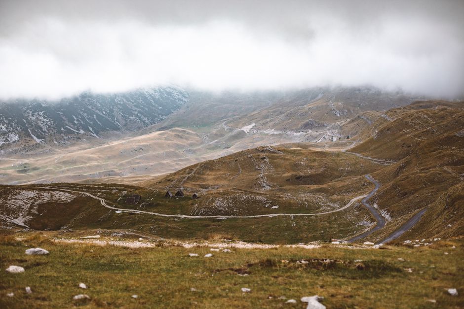 Serene mist-covered mountain landscape with winding road and cloudy sky.