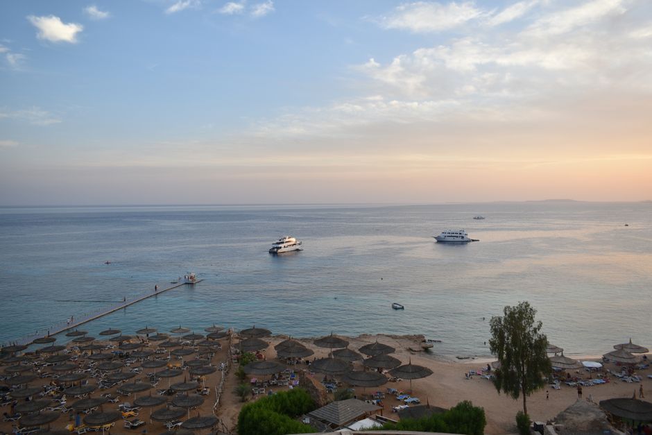 Stunning aerial view of Sharm El Sheikh's beach and sea during sunset with boats and parasols.