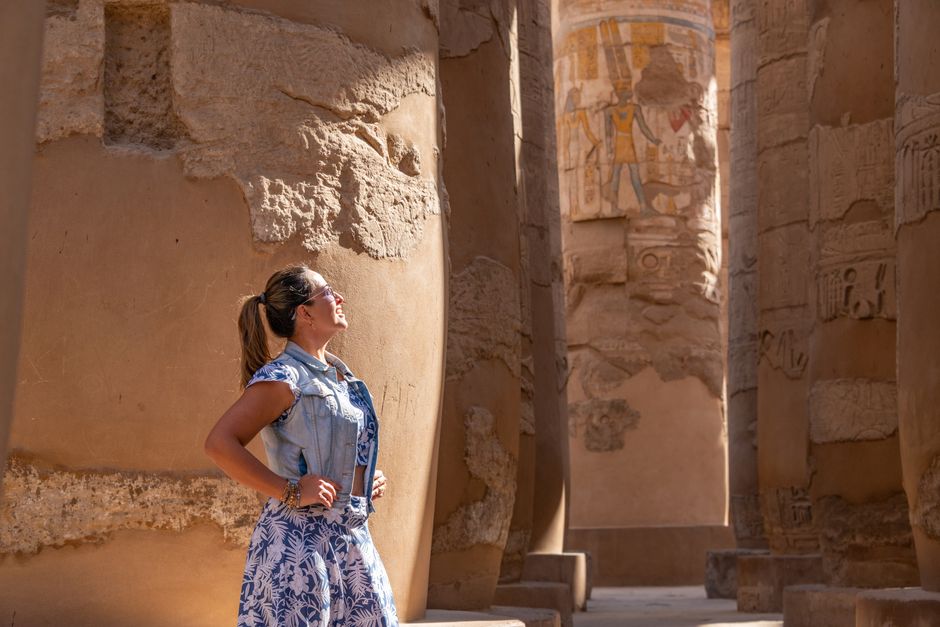 Woman in Luxor Temple admiring ancient carved columns in sunlight.