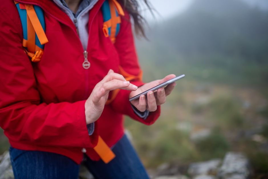 Close-up of a hiker in Portugal using a smartphone outdoors on a foggy day.
