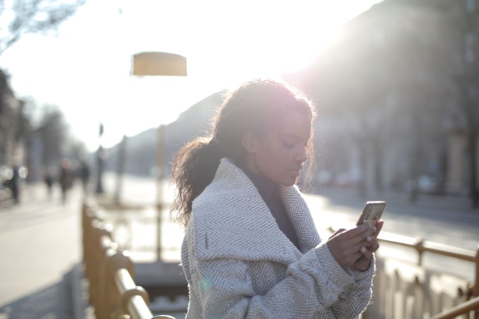 A woman in a winter coat texting on her phone in a city street during daylight.