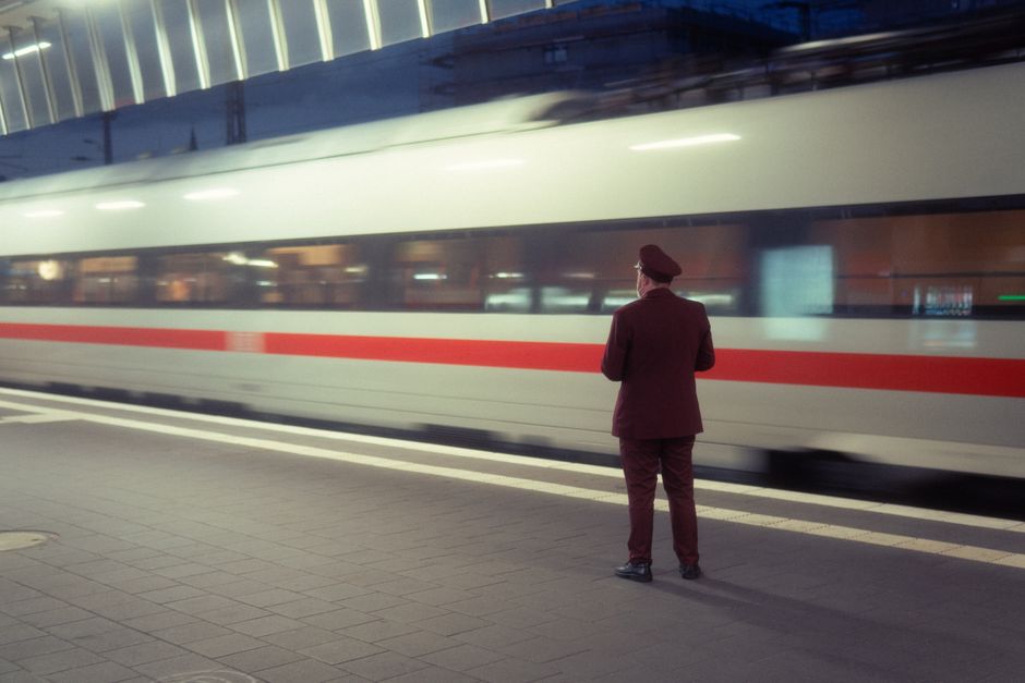 A train conductor observes a high-speed train at a modern station platform in Münster at twilight.
