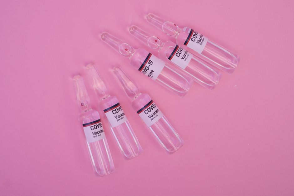 Top view set of sealed glass ampoules with COVID 19 vaccine arranged on pink surface