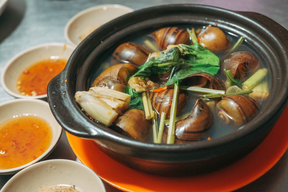 Tasty Vietnamese snail hotpot in clay pot with fresh herbs and dipping sauces, perfect for seafood lovers.