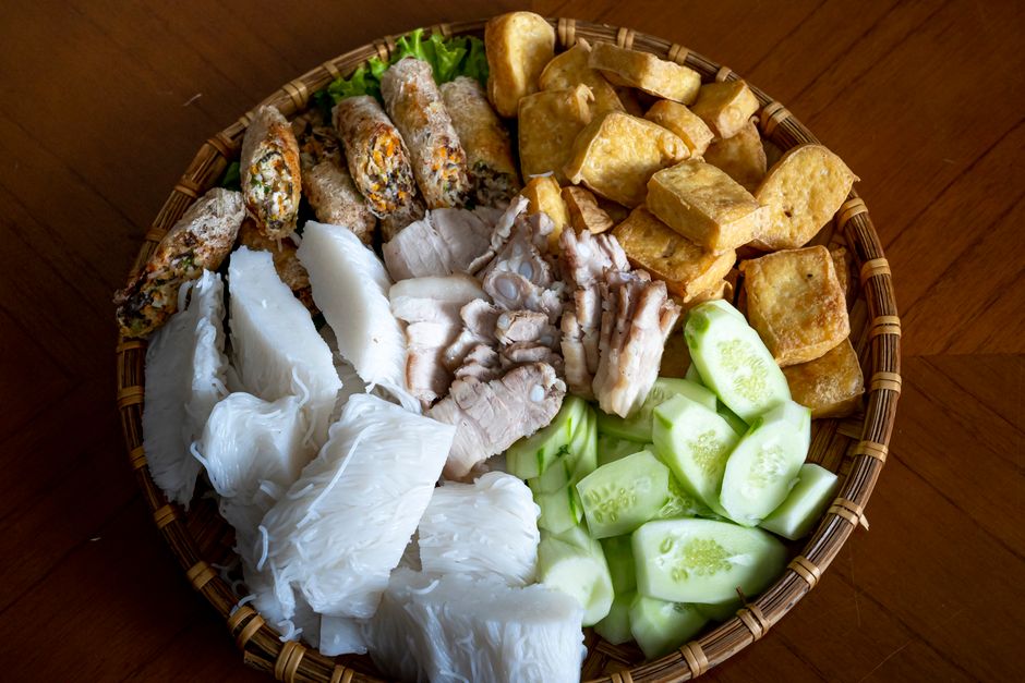 Top view of Asian food with rice noodles cucumber fried tofu and boiled pork with springs rolls served in bowl on table