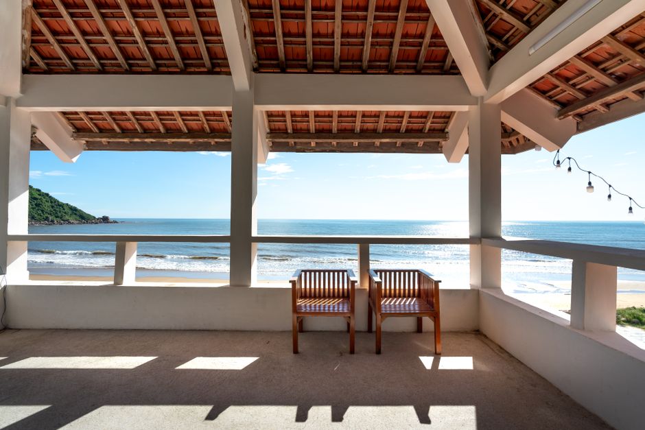 Relaxing wooden chairs overlooking a serene ocean view from a shaded coastal patio.
